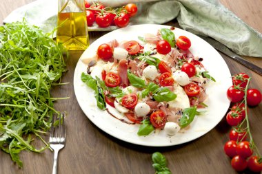 Plate of healthy classic caprese salad with ripe tomatoes and mozzarella cheese with fresh basil leaves on white wooden background clipart