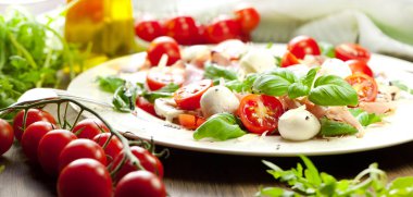 Beyaz ahşap zemin üzerine tabak sağlıklı klasik caprese salatası ile olgun domates ve mozzarella peyniri ile taze fesleğen yaprakları