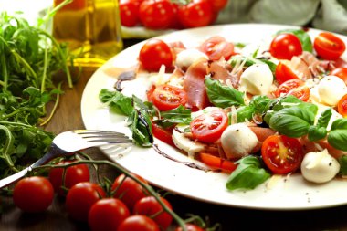 Beyaz ahşap zemin üzerine tabak sağlıklı klasik caprese salatası ile olgun domates ve mozzarella peyniri ile taze fesleğen yaprakları