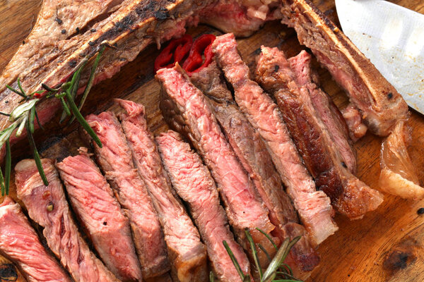 T-bone steak seasoned with spices and fresh herbs served on a wooden board