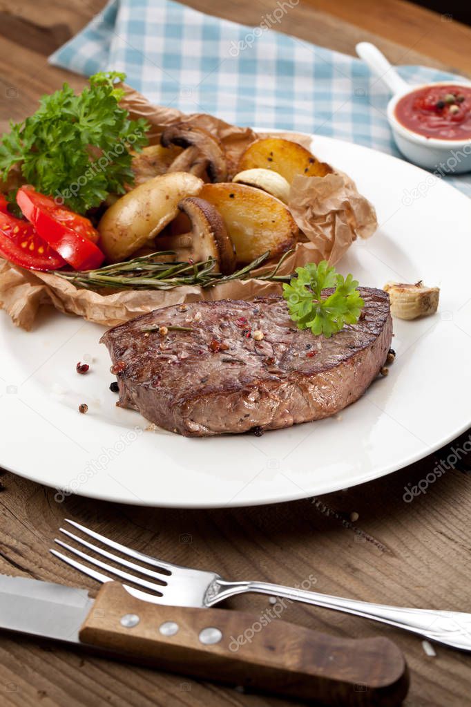 Overhead view of delicious,grilled beef steak with roasted potatoes and fresh green herb salad on an old wooden table