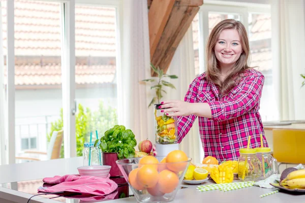 Young smiling woman making smoothie with fresh greens in the blender in kitchen at home.