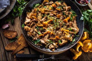 Kırsal siyah ahşap bir masada, dökme demir bir tavada kızarmış mantarlar.