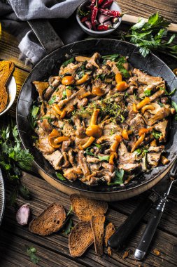 Kırsal siyah ahşap bir masada, dökme demir bir tavada kızarmış mantarlar.