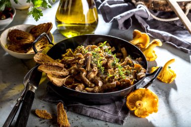 Kırsal siyah ahşap bir masada, dökme demir bir tavada kızarmış mantarlar.