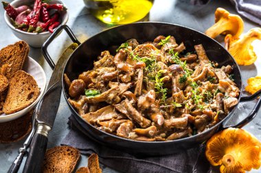 Kırsal siyah ahşap bir masada, dökme demir bir tavada kızarmış mantarlar.