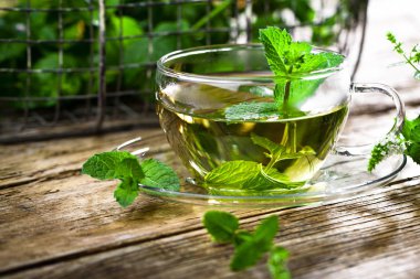 Bir fincan sıcak çay, kamış şekeri, çay yaprakları ve nane bitkisi..