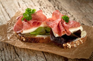 Baharatlı İtalyan salam sosis ve eski grunge rustik ahşap tahta üzerinde salata ile tepesinde tohumları ile kepekli ekmek