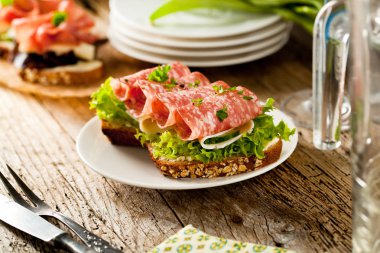 Baharatlı İtalyan salam sosis ve eski grunge rustik ahşap tahta üzerinde salata ile tepesinde tohumları ile kepekli ekmek