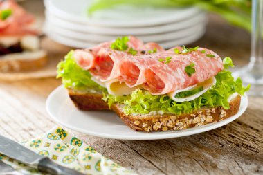 Baharatlı İtalyan salam sosis ve eski grunge rustik ahşap tahta üzerinde salata ile tepesinde tohumları ile kepekli ekmek