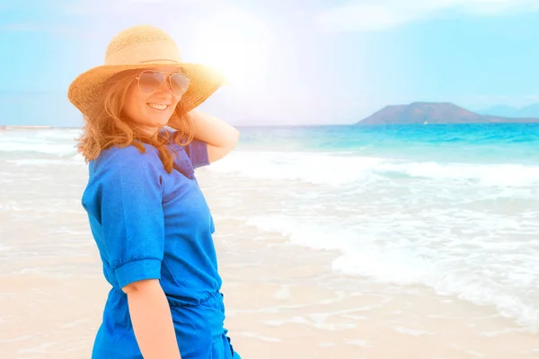 Happy traveller woman in blue dress enjoys her tropical beach vacation