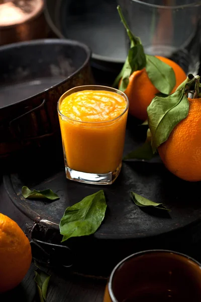 stock image Orange smoothie and orange fruits with green leaves on dark background