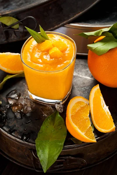 Orange smoothie and orange fruits with green leaves on dark background