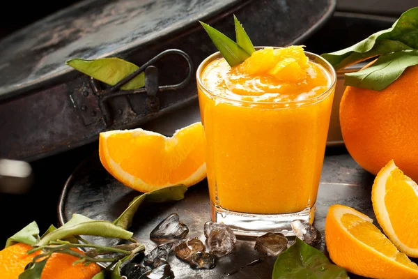 Orange smoothie and orange fruits with green leaves on dark background