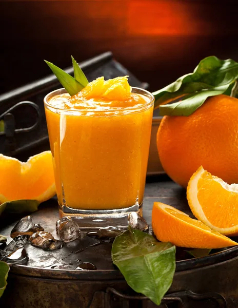 Orange smoothie and orange fruits with green leaves on dark background