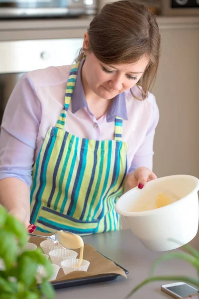 Charming woman baking in the kitchen at home blueberry muffins.