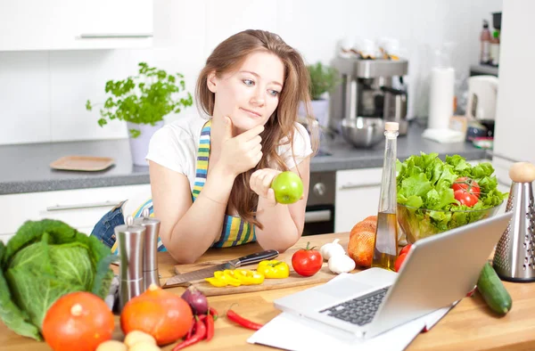 Cooking woman looking at computer while preparing food in kitchen