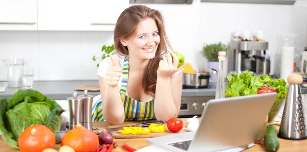 Cooking woman looking at computer while preparing food in kitchen