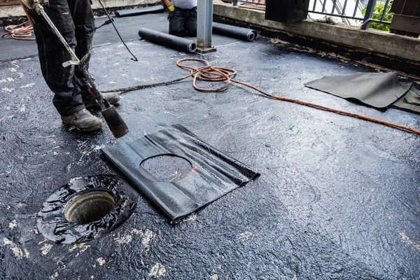 Flat roof installation. Heating and melting bitumen roofing felt.