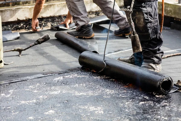 Flat roof installation. Heating and melting bitumen roofing felt.