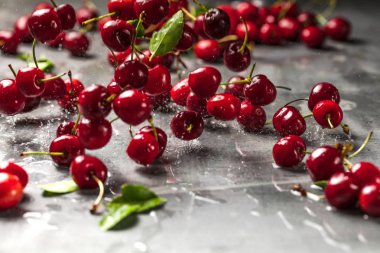 Olgun kiraz yığınını yaprak ve saplarla kapatın. Büyük bir taze kırmızı kiraz koleksiyonu. Olgun kiraz arkaplanı