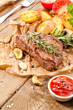 Lezzetli, ızgara sığır eti biftek ile kızarmış patates ve taze yeşil ot salatası havai görünümü eski ahşap masa