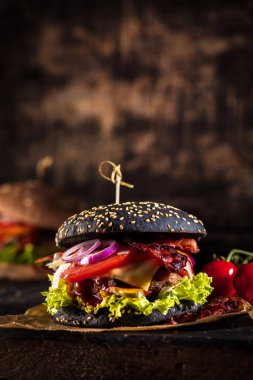Siyah burger patty et, peynir, domates, mayonez. Koyu ahşap rustik masa. Modern hızlı yiyecek öğle yemeği.