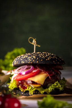 Siyah burger patty et, peynir, domates, mayonez. Koyu ahşap rustik masa. Modern hızlı yiyecek öğle yemeği.