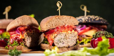 Siyah burger patty et, peynir, domates, mayonez. Koyu ahşap rustik masa. Modern hızlı yiyecek öğle yemeği.