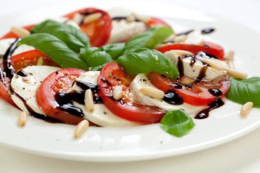 Beyaz ahşap zemin üzerine tabak sağlıklı klasik lezzetli caprese salatası ile olgun domates ve mozzarella peyniri ile taze fesleğen yaprakları