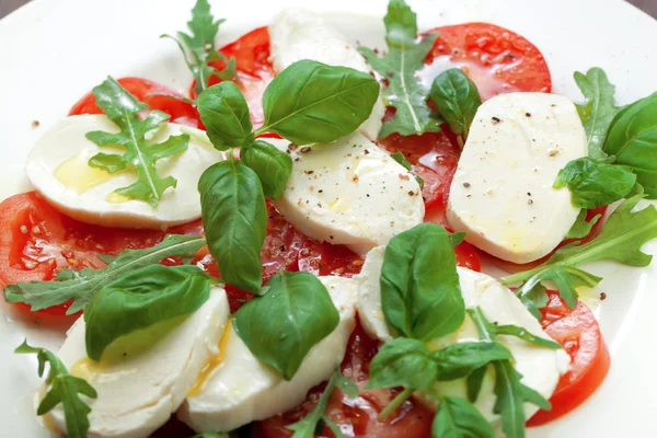 Beyaz ahşap zemin üzerine tabak sağlıklı klasik lezzetli caprese salatası ile olgun domates ve mozzarella peyniri ile taze fesleğen yaprakları