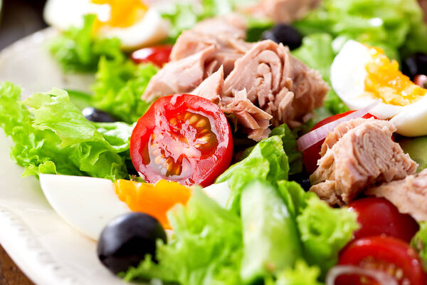 Tuna salad with lettuce, eggs and tomatoes on dark wooden table