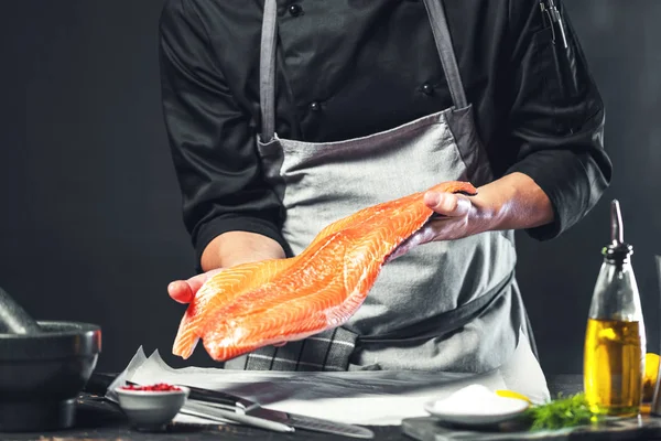 The big salmon is in the hands of the chef cook. He is using a knife to slice salmon fillet