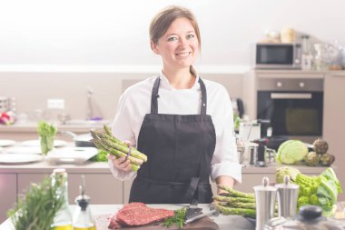 Üniformalı, gülümseyen kadın mutfakçı restoranın mutfağında duruyor..