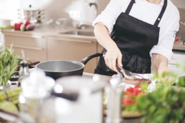 Üniformalı, gülümseyen kadın mutfakçı restoranın mutfağında duruyor..