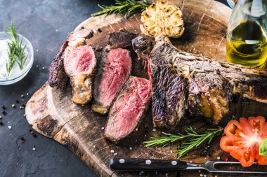 Taze biberiye ve domates görünümü kadar yakın bir kalbur üzerinde nadir ızgara veya mangalda tomahawk sığır eti biftek dilimlenmiş
