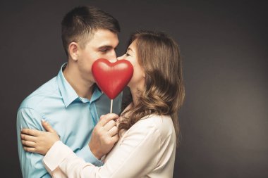 Gri duvarının yakınında kırmızı balon şeklinde kalbi olan genç çift