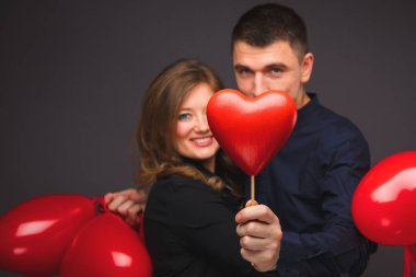 Gri duvarının yakınında kırmızı balon şeklinde kalbi olan genç çift