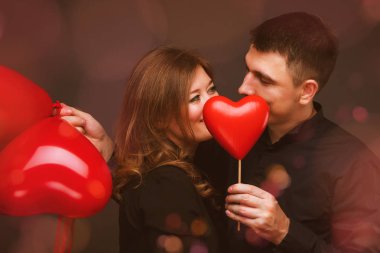 Gri duvarının yakınında kırmızı balon şeklinde kalbi olan genç çift