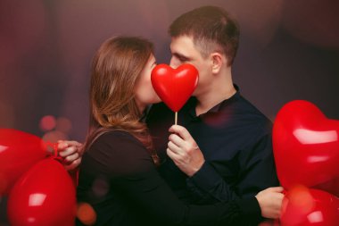 Gri duvarının yakınında kırmızı balon şeklinde kalbi olan genç çift