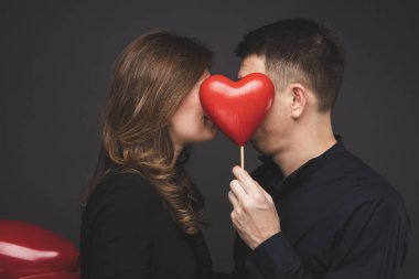 Gri duvarının yakınında kırmızı balon şeklinde kalbi olan genç çift