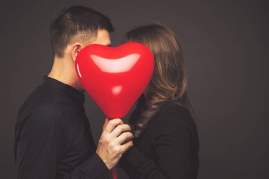 Gri duvarının yakınında kırmızı balon şeklinde kalbi olan genç çift