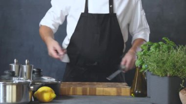 Önlüklü erkek aşçının mutfakta bıçak keskinleştirdiği keskinleştirilmiş bir fotoğraf.
