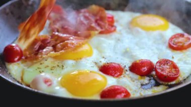 Domuz pastırmalı, domatesli ve fesleğenli yumurta pişiren kişinin yakın plan görüntüsü.   