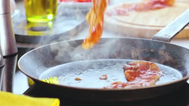 vue rapprochée de la personne qui cuisine des œufs avec du bacon, des tomates et des feuilles de basilic sur une poêle  
