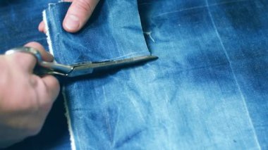 Terzi dikiş makinesine kot pantolon dikiyor, manzarayı kapatıyor.