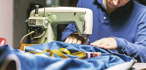Sewing denim jeans with sewing machine. Repair jeans by sewing machine. Alteration jeans, hemming a pair of jeans, handmade garment industrial concept