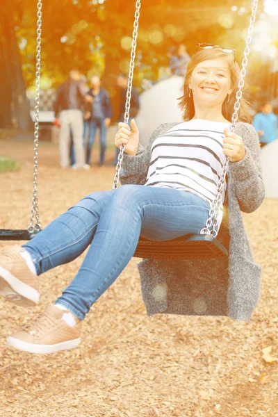 Όμορφη Χαμογελαστή Γυναίκα Στηρίζεται Swing Στην Παιδική Χαρά — Φωτογραφία Αρχείου