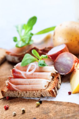 Ekmek, dilimlenmiş et, peynir, baharat ve sebzelerin ahşap masada yakın plan görüntüsü.