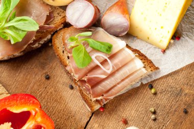 Ekmek, dilimlenmiş jambon, peynir, baharat ve sebzeli ahşap masada nefis yemek manzarası.